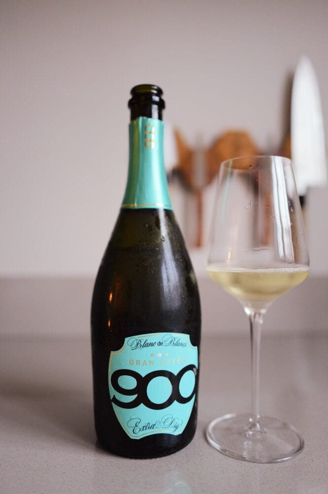 900 Gran Cuvée Blanc de Blancs bottle with a turquoise label beside a glass of sparkling wine