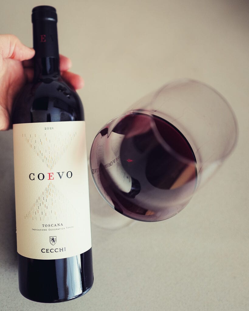 Hand houdt fles Cecchi Coevo 2021 vast naast een gekanteld glas rode wijn