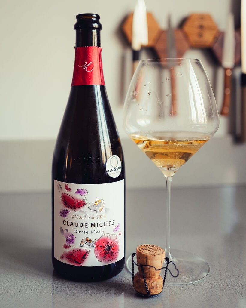 Fles Champagne Claude Michez Cuvée Flore met bloemen-etiket naast een glas en een kurk