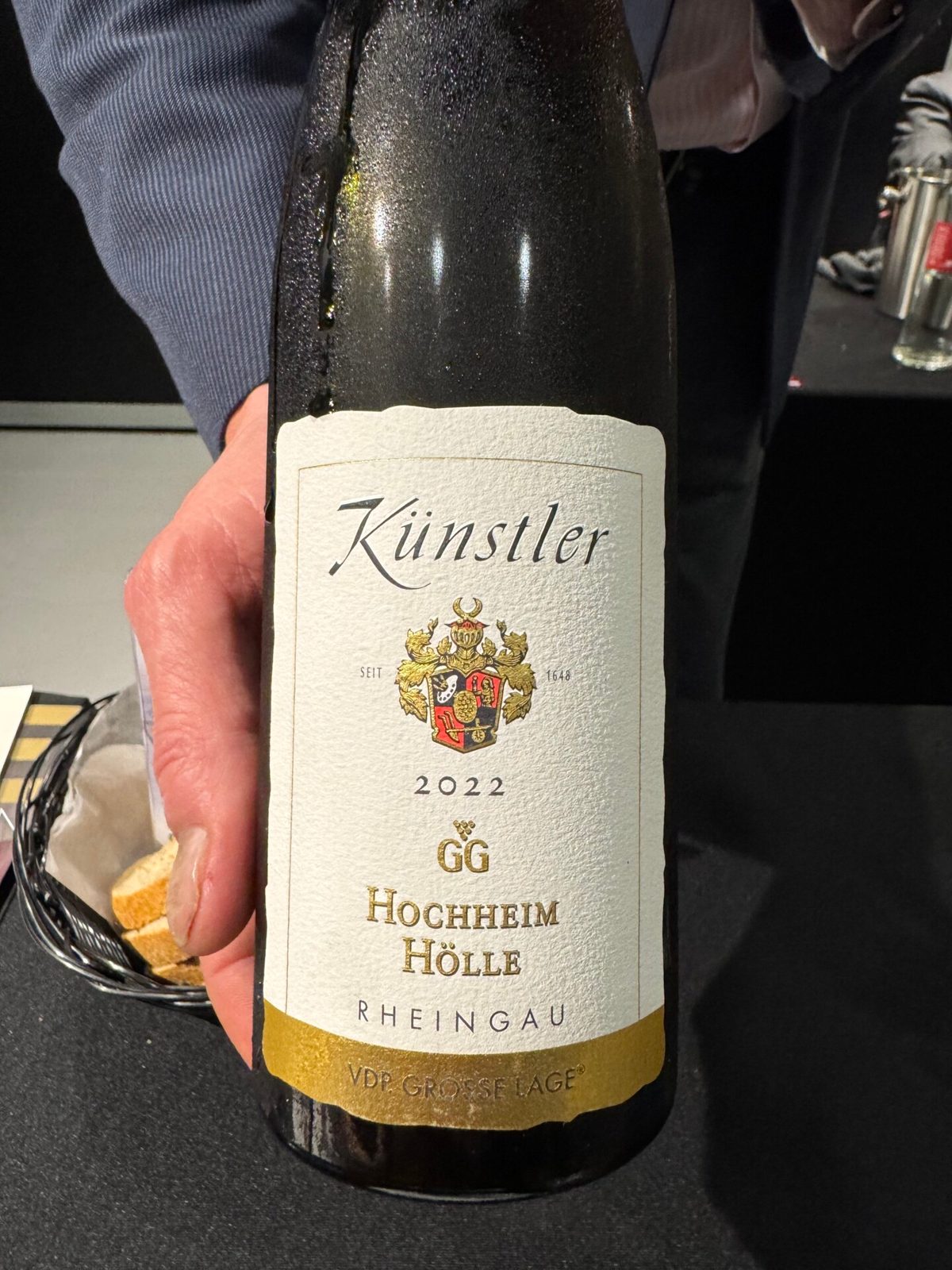 Fles Künstler 2021 GG Hochheim Hölle Riesling met wapen-etiket, vastgehouden in een donkere zaal
