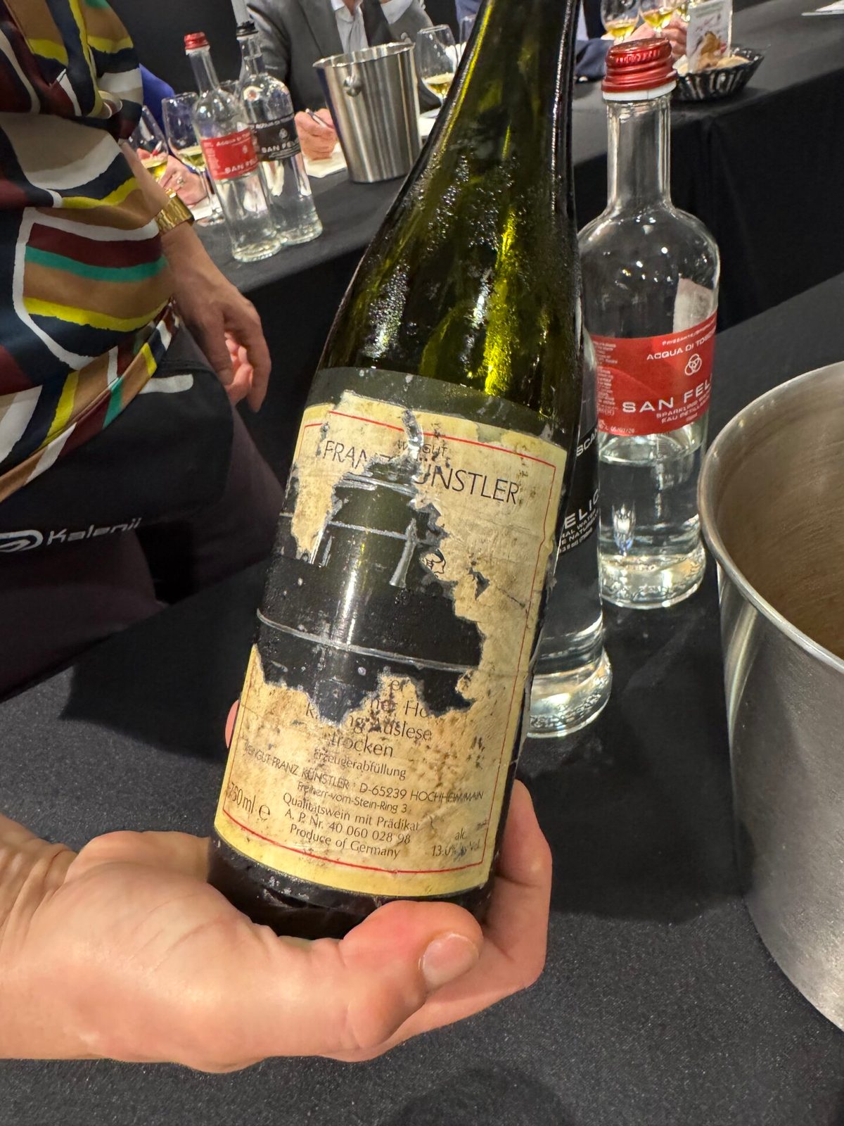Oude fles Franz Künstler Hölle Auslese met versleten, gehavend etiket, vastgehouden naast waterflessen