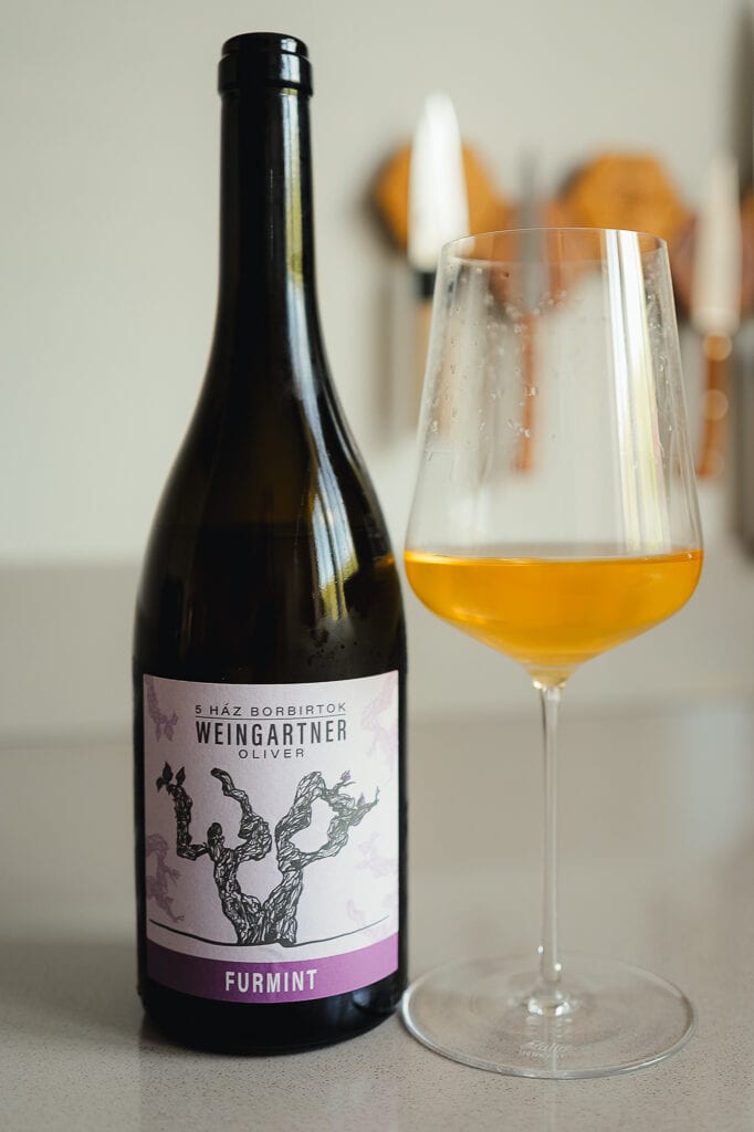 Fles Weingartner Oliver Furmint naast glas troebele amberkleurige oranjewijn