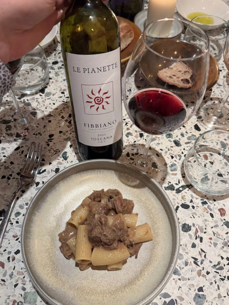 Fibbiano Le Pianette Toscana red wine bottle beside a plate of rigatoni and a glass of red