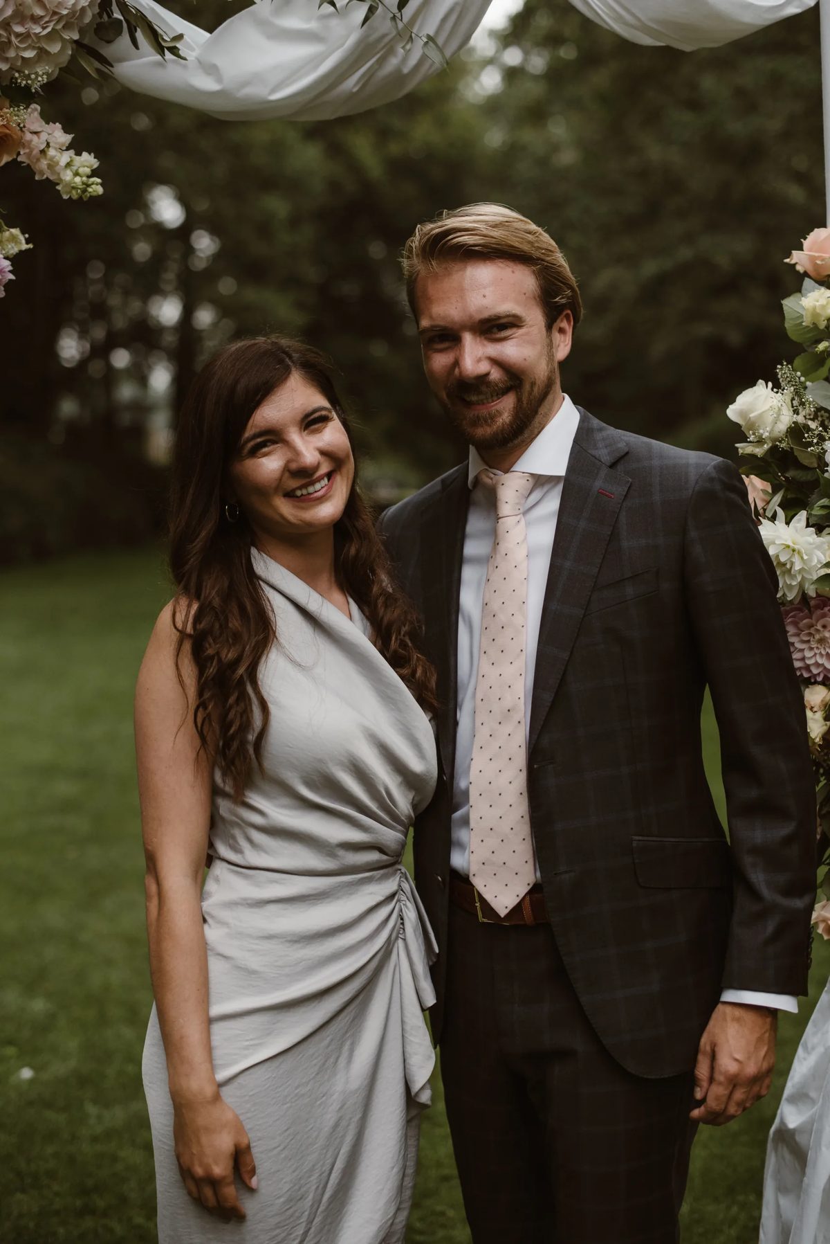 Smiling couple posing together at an outdoor wedding with flowers and greenery