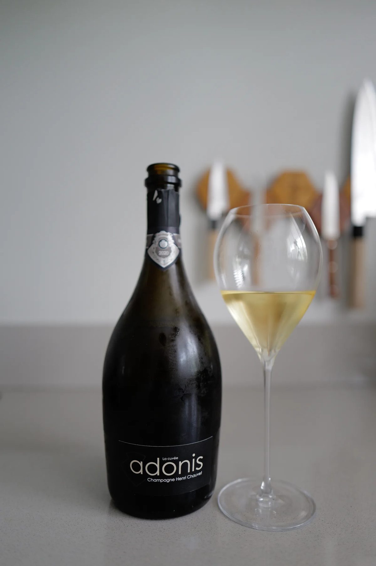 Bottle of Henri Chauvet Adonis 2020 next to a glass of champagne