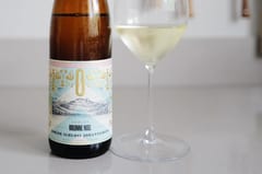 Fles Kolonne Null Gelblack alcoholvrije Riesling naast een glas witte wijn op een licht keukenblad