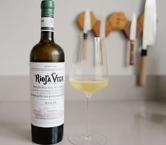 Fles Rioja Vega Maturana Blanca 2025 met een glas witte wijn op een keukenblad, Japanse messen aan de wand