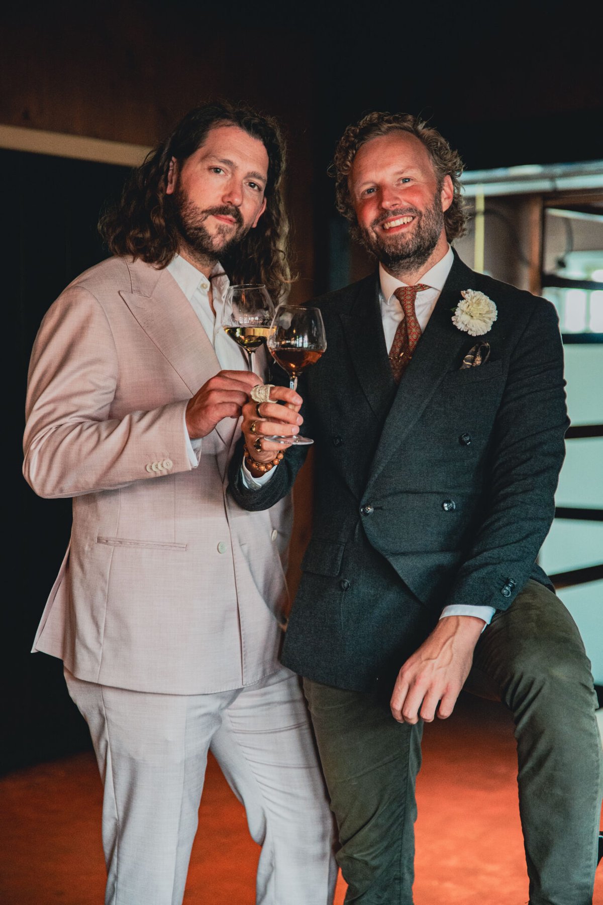 Twee glimlachende mannen in pak proosten met glazen sherry, tegen een warme oranje achtergrond
