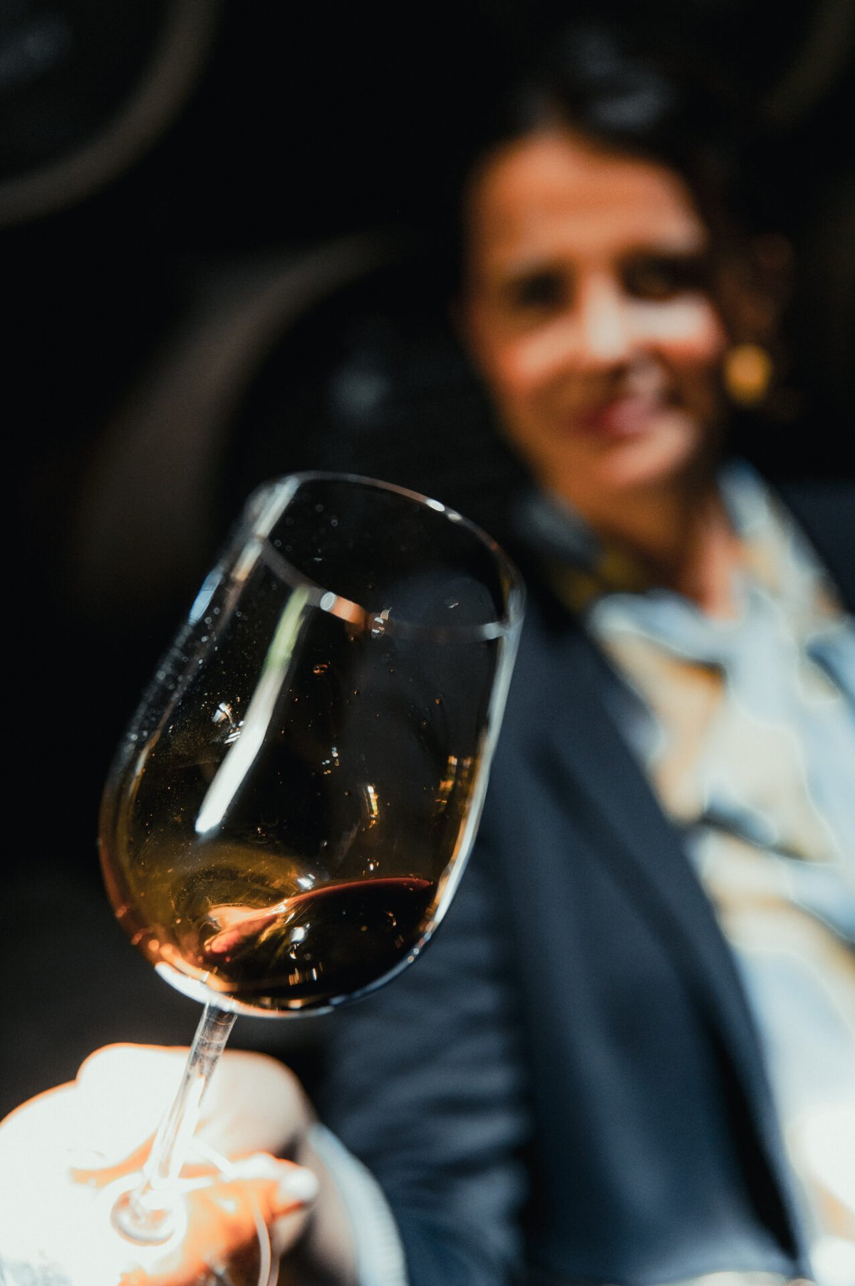 Close-up van een glas donkere amberkleurige sherry, met een glimlachende vrouw onscherp op de achtergrond