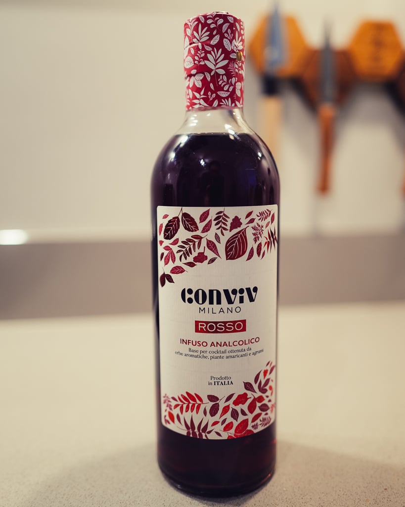Fles Conviv Milano Rosso met rood bloemmotief-etiket naast een tumbler met amberkleurige drank en ijs