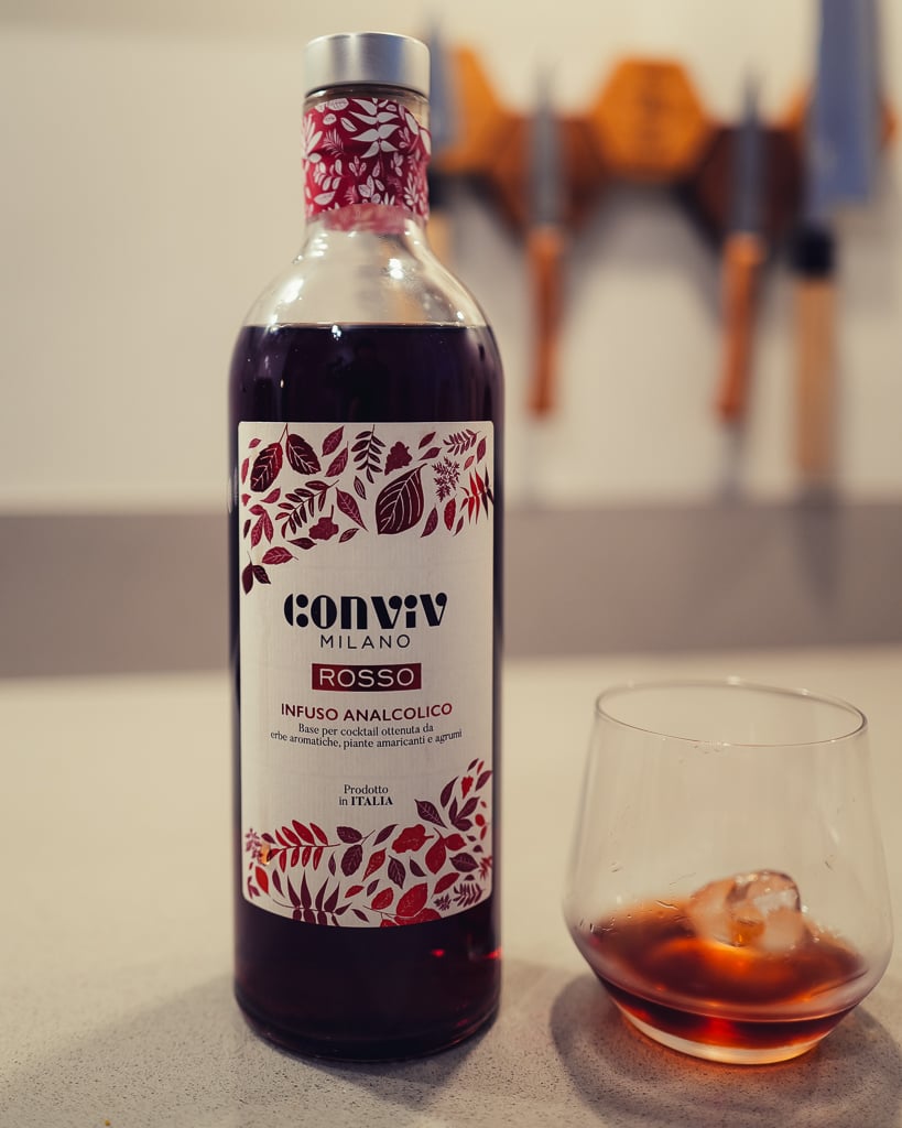 Fles Conviv Milano Rosso met zilveren dop naast een tumbler met rode drank en een ijsblokje