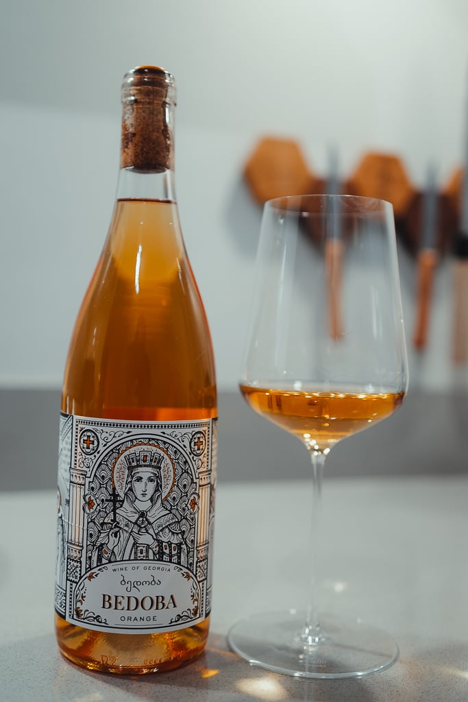Fles Bedoba Orange uit Georgië met een iconisch heiligenportret op het etiket, naast een glas amberkleurige wijn
