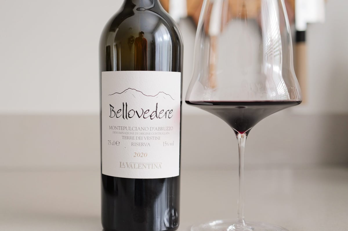 Fles Bellovedere 2020 naast een ruim glas rode wijn met diepe robijnrode kleur op een lichte ondergrond