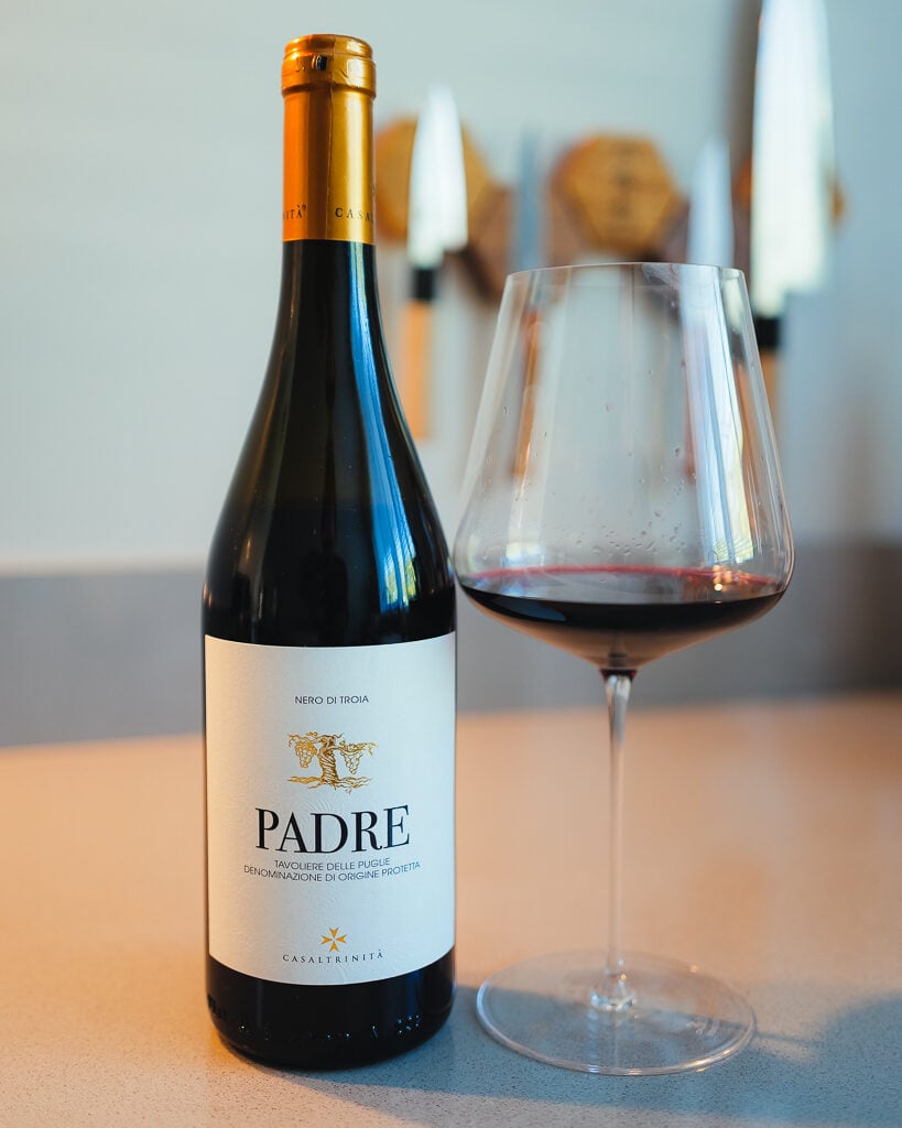 Fles Padre Nero di Troia van Casaltrinita met gouden capsule naast een glas rode wijn op een aanrecht