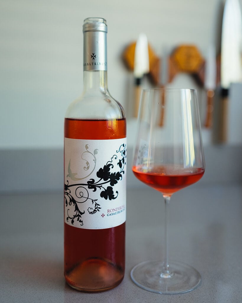 Fles Rondirosa rosé van Casaltrinita met bloemig etiket naast een glas zalmroze wijn op een aanrecht