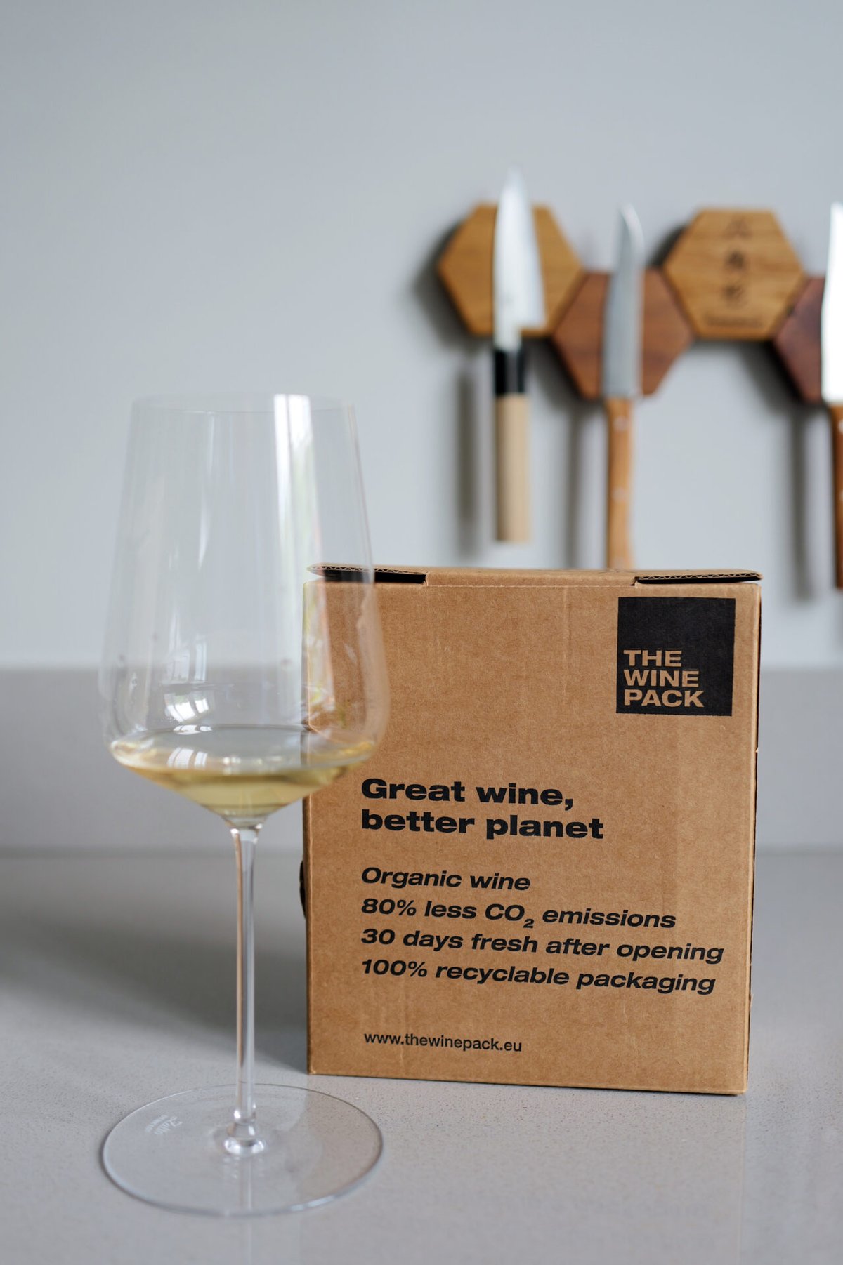 Glas witte wijn naast een kartonnen The Wine Pack-doos met de tekst Great wine, better planet