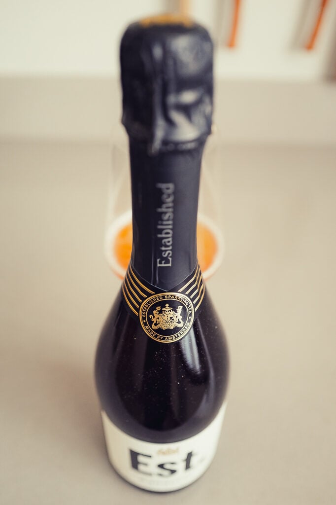 Dark foiled neck of the Est. sparkling tea bottle with gold seal, glass behind