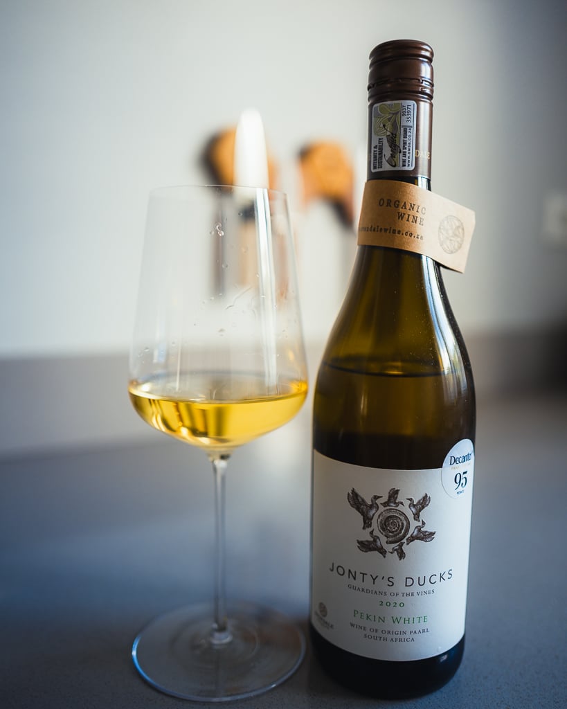 Fles Jonty's Ducks Pekin White uit Zuid-Afrika naast een glas goudgele witte wijn op een aanrecht