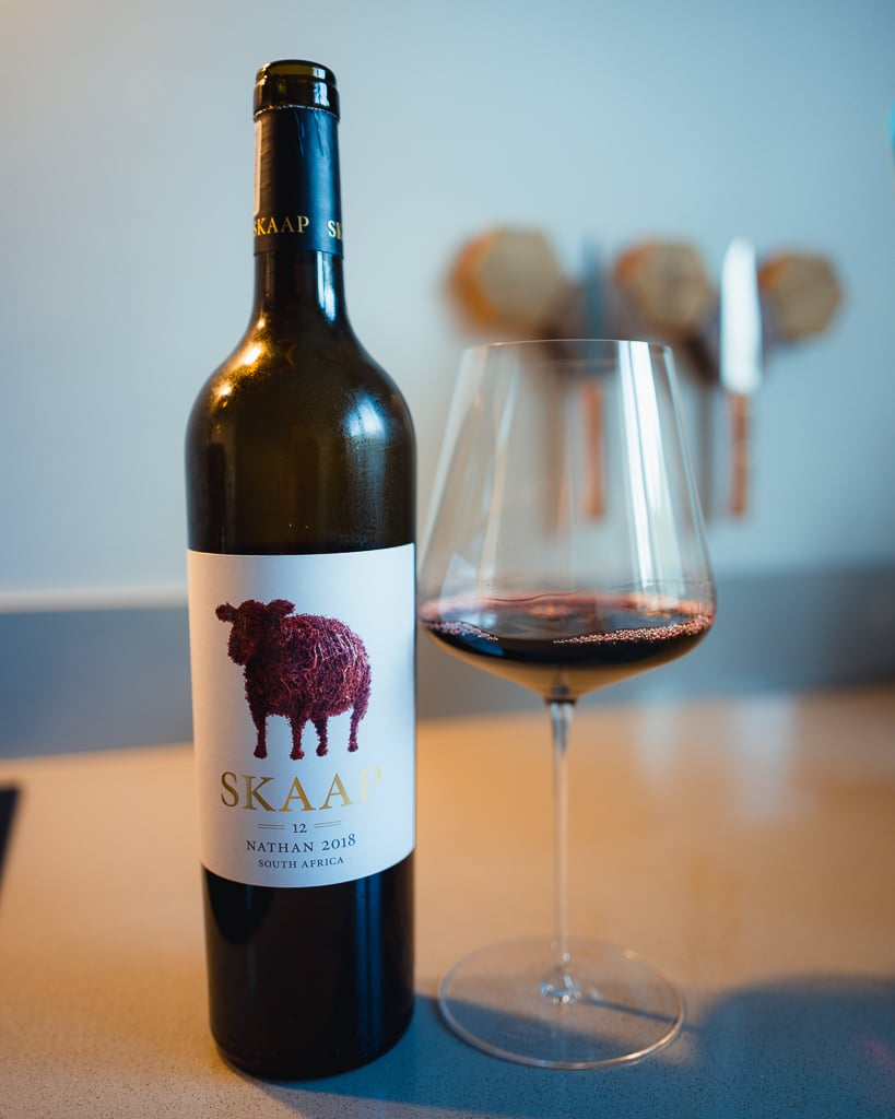 Fles Skaap Nathan 2018 uit Stellenbosch met schaap-illustratie op het etiket naast een glas rode wijn