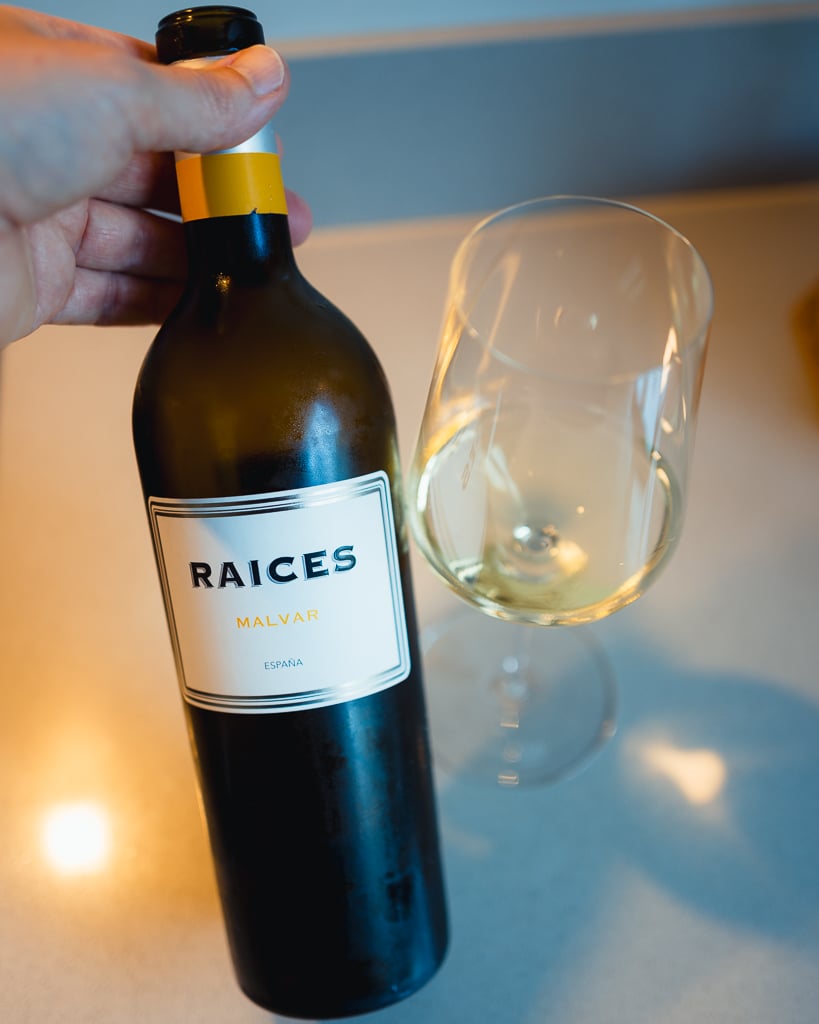 Hand houdt fles Raíces Malvar witte wijn vast naast een glas witte wijn