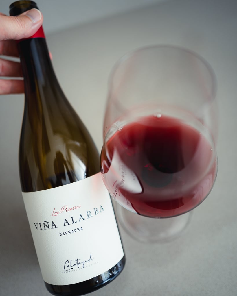 Hand houdt fles Las Pizarras Viña Alarba Garnacha vast boven een glas rode wijn