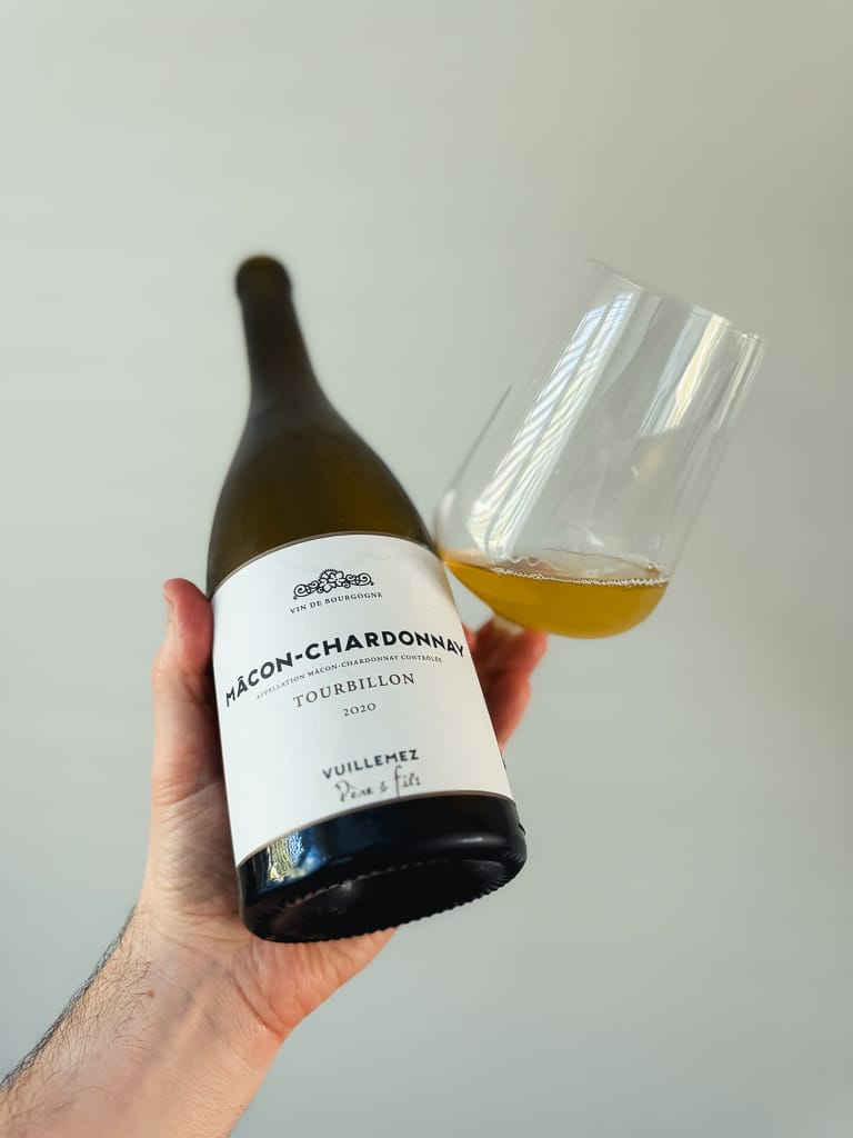Hand houdt fles Mâcon-Chardonnay Tourbillon 2020 vast naast een glas witte wijn