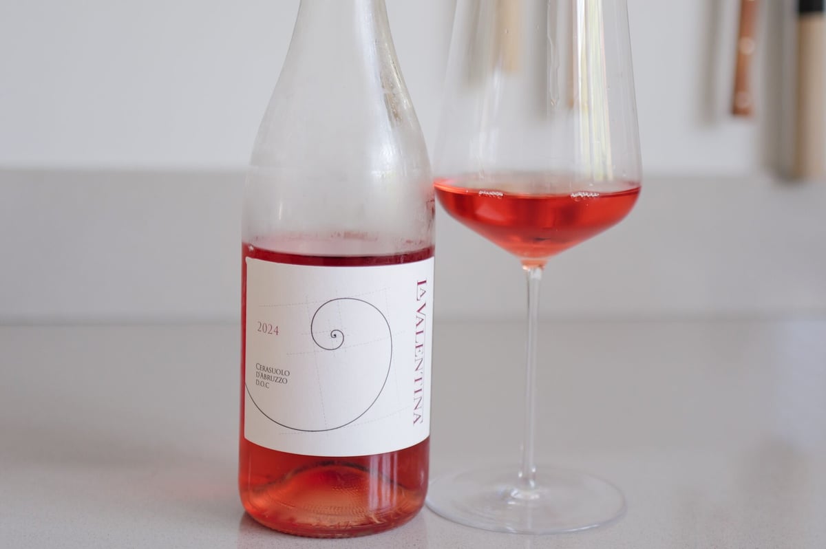 Fles La Valentina Cerasuolo d'Abruzzo 2024 met spiraal-etiket naast een glas kersrode rosé