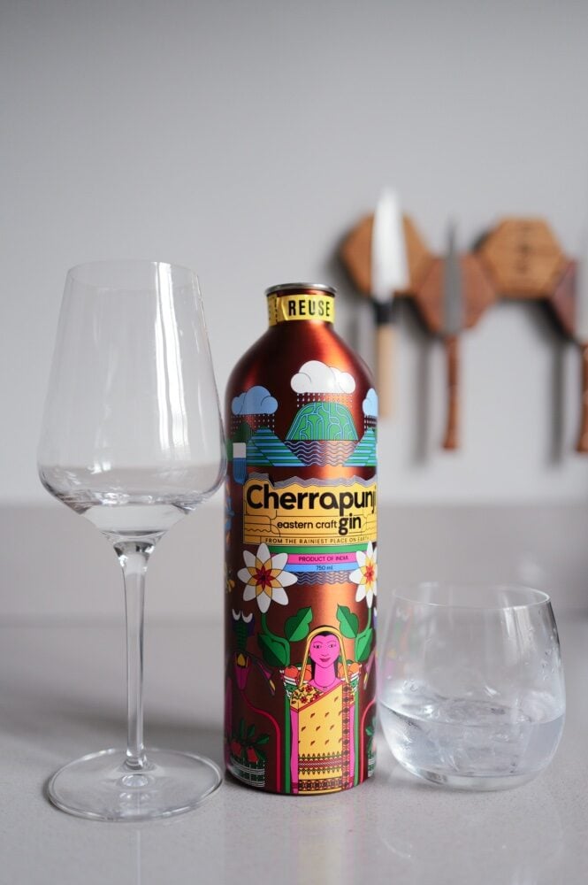 Kleurrijk beschilderd blik Cherrapunji craft gin uit India naast een wijnglas en een tumbler met ijs