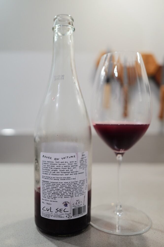Achterkant van de fles Cul Sec Rouge en Voiture met proefnotities naast een glas rode wijn