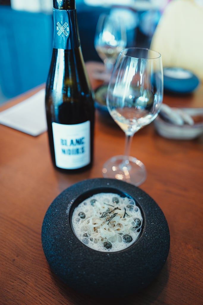 Fles Blanc Noirs champagne naast een gerecht met schuim in een donkere kom