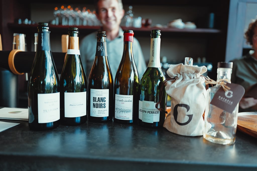 Vijf champagneflessen waaronder Blanc Noirs en Joseph Perrier op de bar, gastheer op de achtergrond
