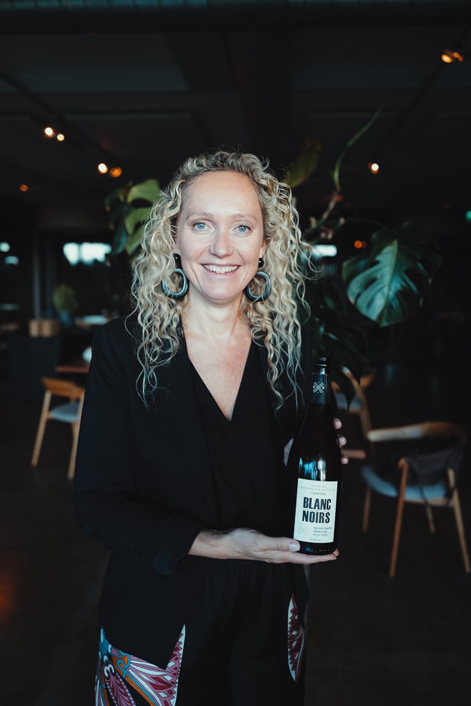 Vrouw met blonde krullen houdt een fles Blanc Noirs champagne vast in het restaurant