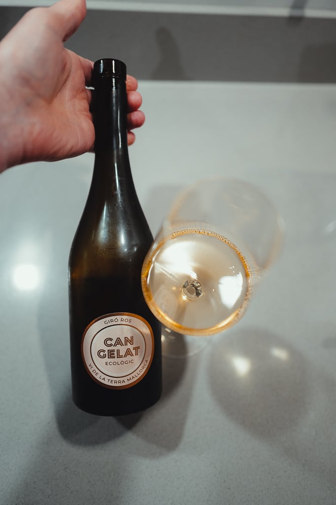 Hand houdt fles Can Gelat Giró Ros vast naast een liggend glas oranjewijn