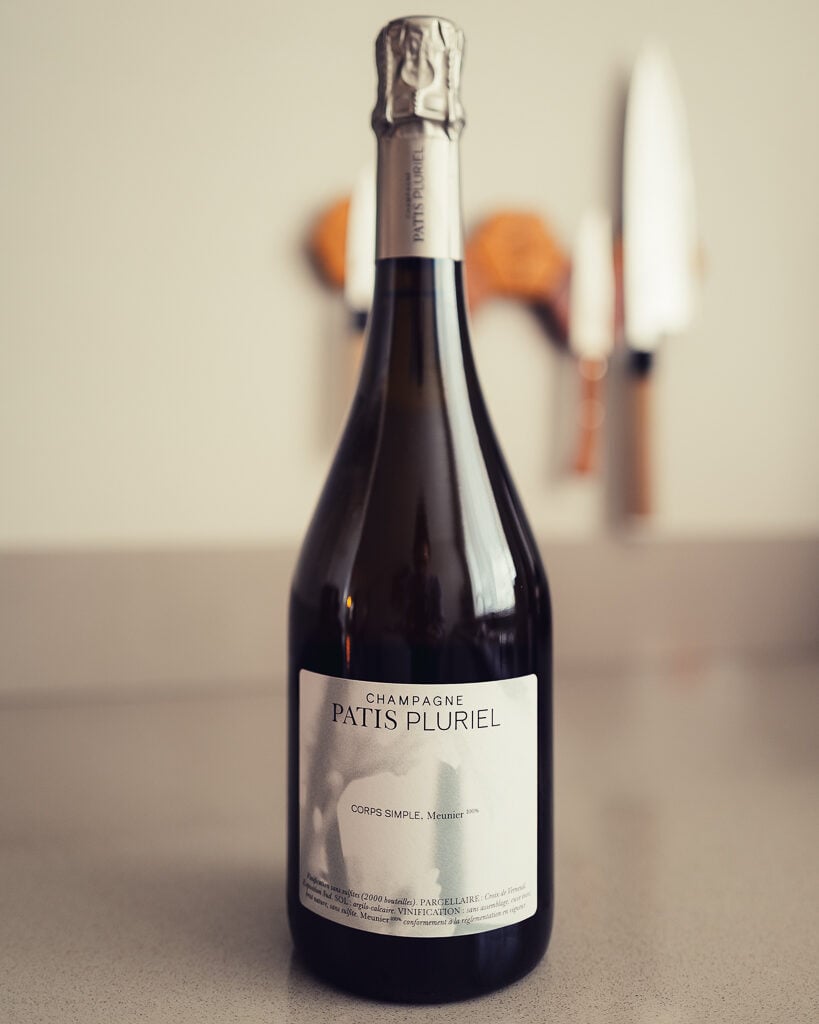Fles Champagne Patis Pluriel Corps Simple op een aanrecht, messenblok wazig op de achtergrond
