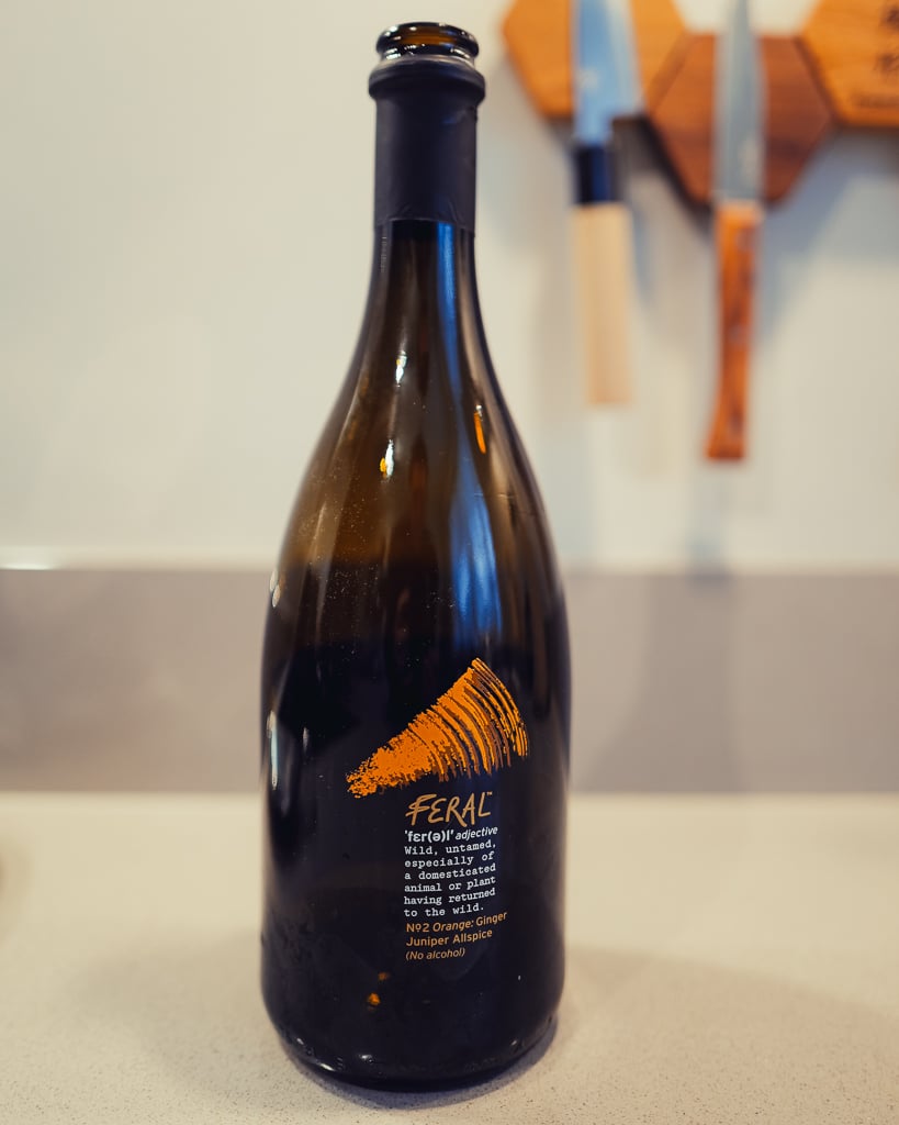 Dark Feral No2 Orange bottle with an orange brushstroke label on a counter, knives blurred behind