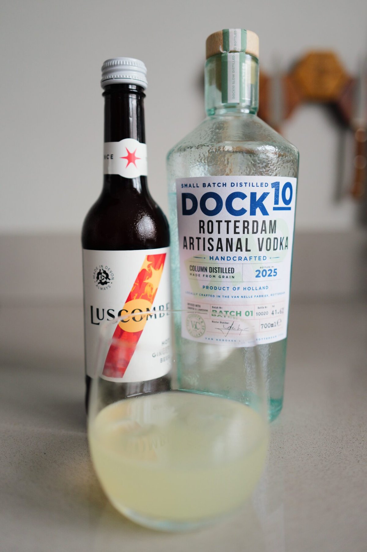 Fles DOCK10 vodka naast een Luscombe-flesje en schaaltje lichtgele cocktail
