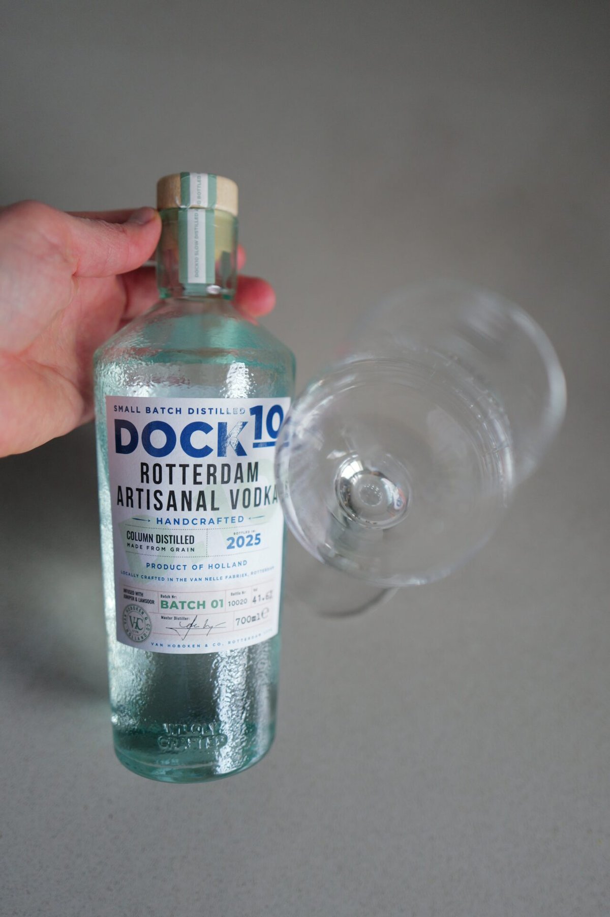 Hand houdt fles DOCK10 Rotterdam Artisanal Vodka vast naast een liggend leeg glas