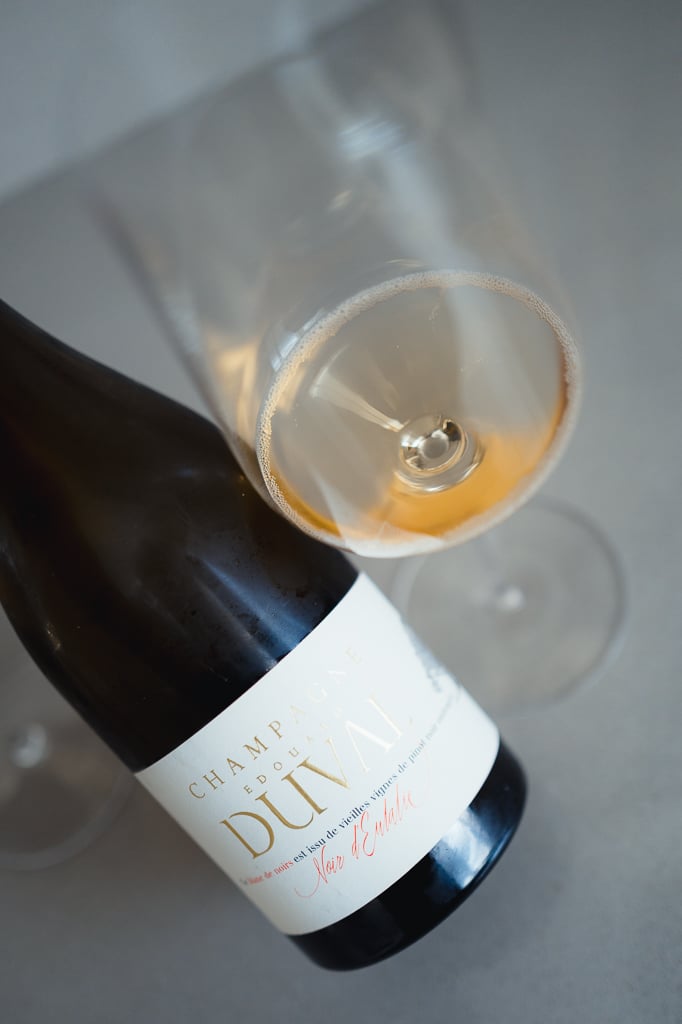 Fles Edouard Duval Noir d'Eulalie ligt naast een glas oranje-getinte champagne van bovenaf gezien