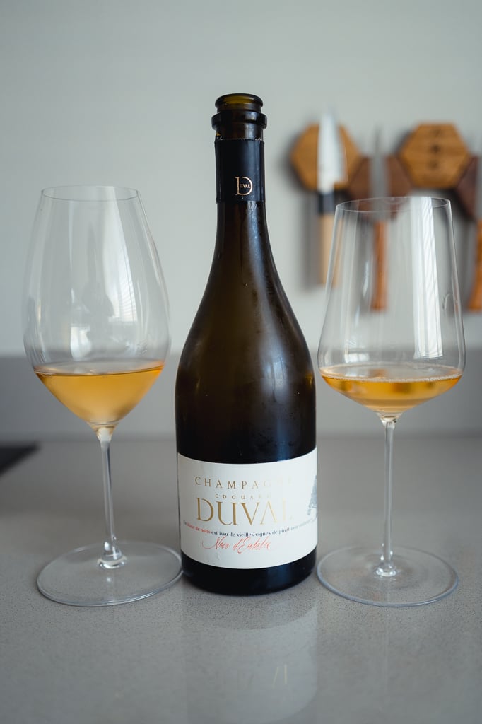Fles Champagne Edouard Duval Noir d'Eulalie tussen twee glazen oranje-getinte champagne