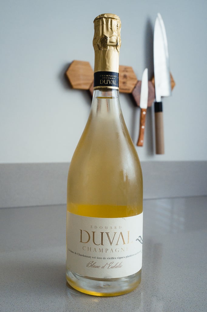 Fles Edouard Duval Blanc d'Eulalie met goudkapsel, messen wazig aan de muur op de achtergrond
