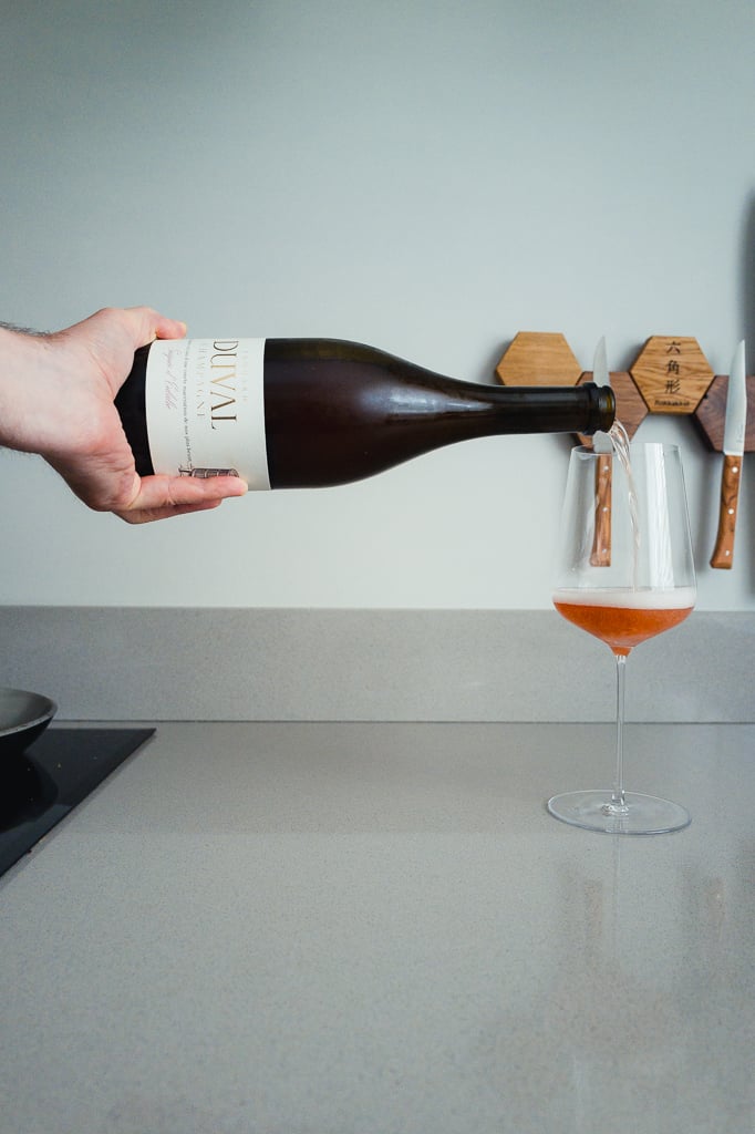 Hand schenkt Edouard Duval champagne in een wijnglas met roze mousse op een aanrecht