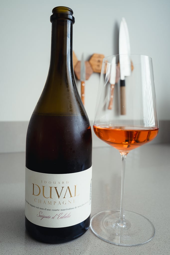 Fles Edouard Duval Saignée d'Eulalie met glas zalmroze champagne, messen wazig op de achtergrond