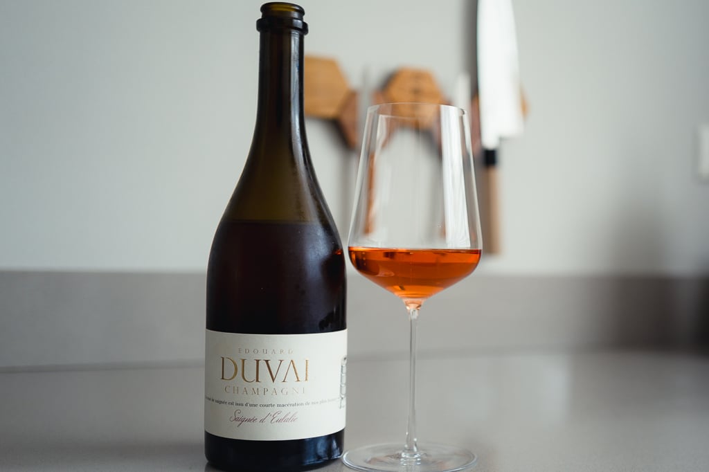 Fles Edouard Duval Saignée d'Eulalie met glas zalmroze champagne op een lichtgrijs aanrecht