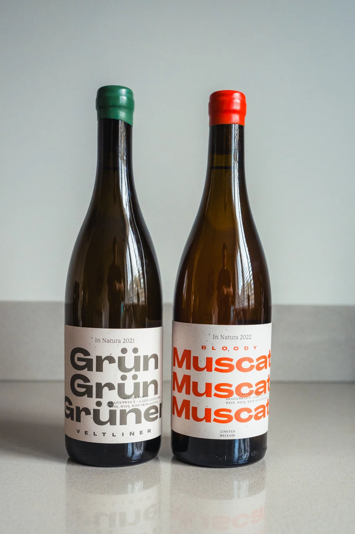Twee flessen naast elkaar: Grün Grüner Veltliner met groen kapsel en Bloody Muscat met rood kapsel