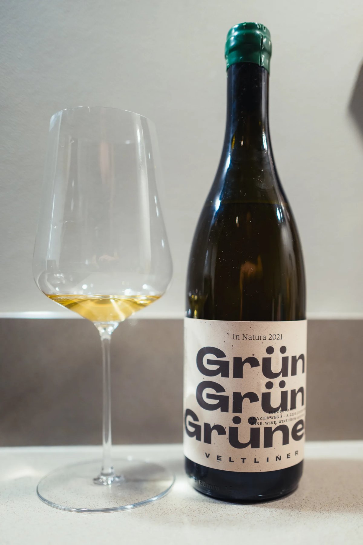 Fles Grün Grün Grüner Veltliner In Natura 2021 met groen kapsel naast glas lichtgele wijn