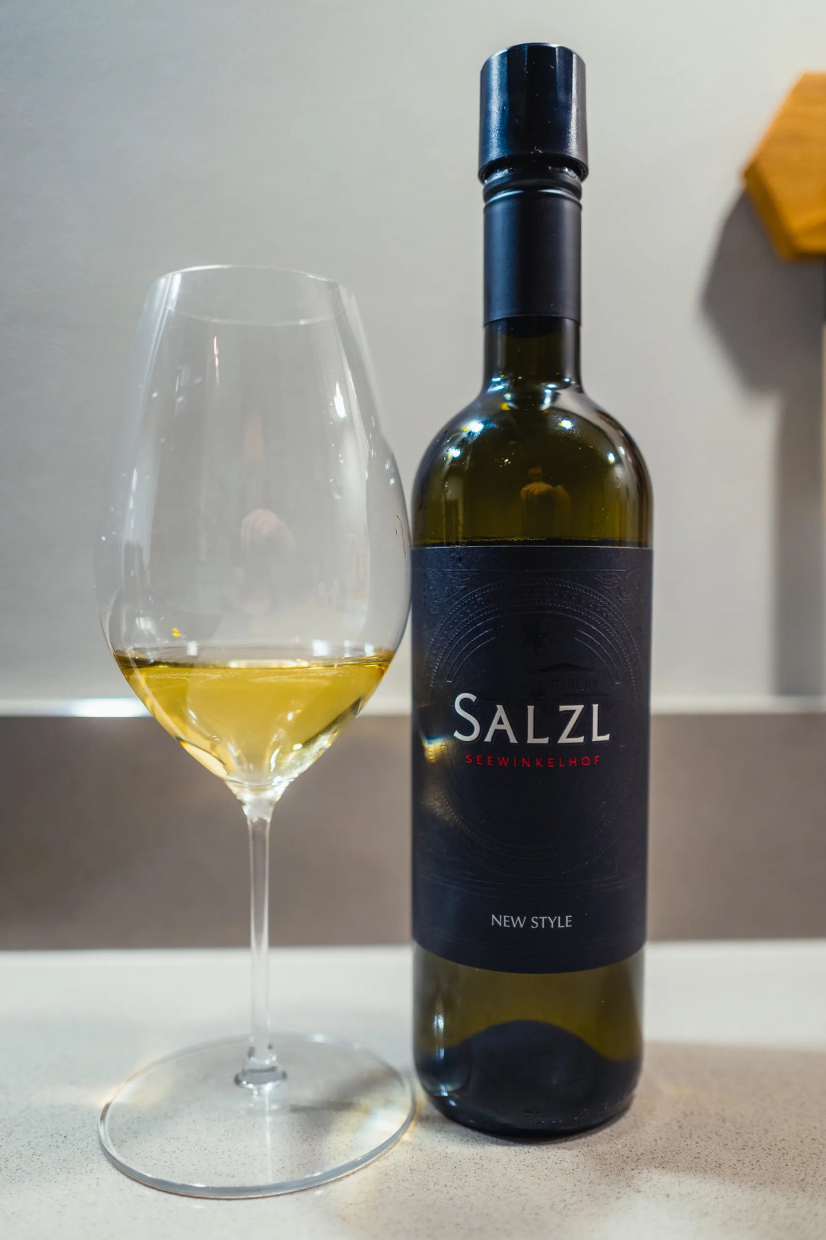 Fles Salzl New Style met zwart etiket naast glas lichtgele wijn