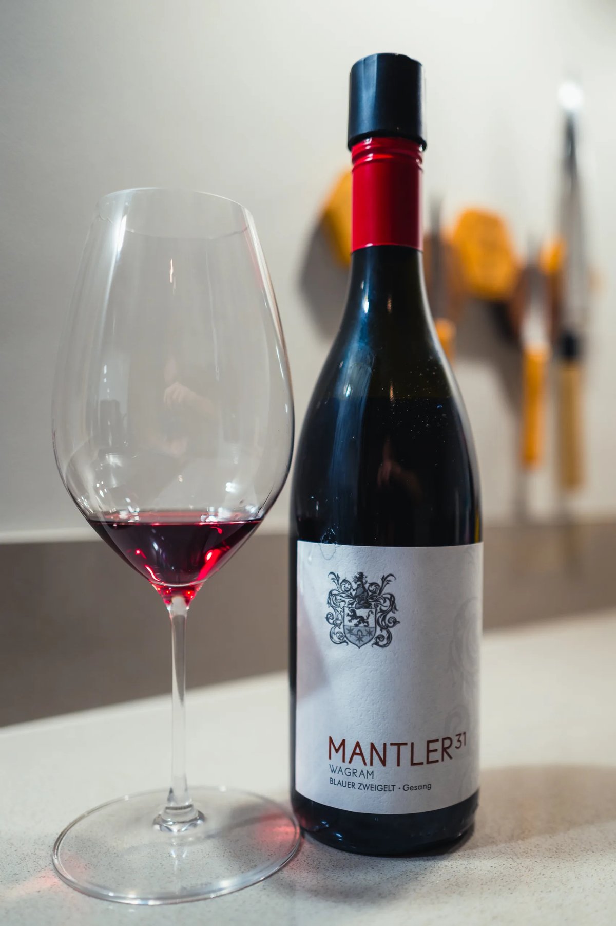 Fles Mantler 31 Blauer Zweigelt uit Wagram met rood kapsel naast glas rode wijn