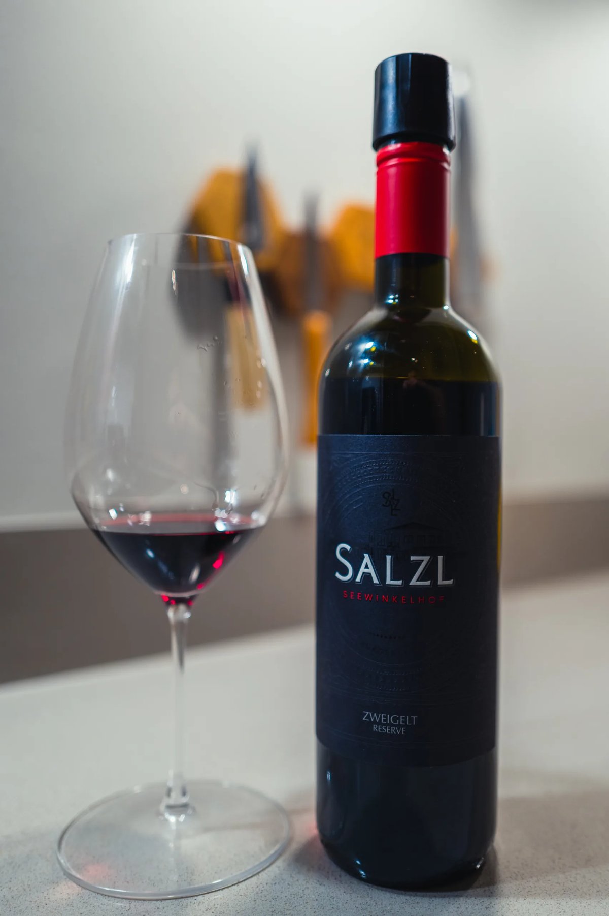 Fles Salzl Zweigelt Reserve met rood kapsel naast glas rode wijn