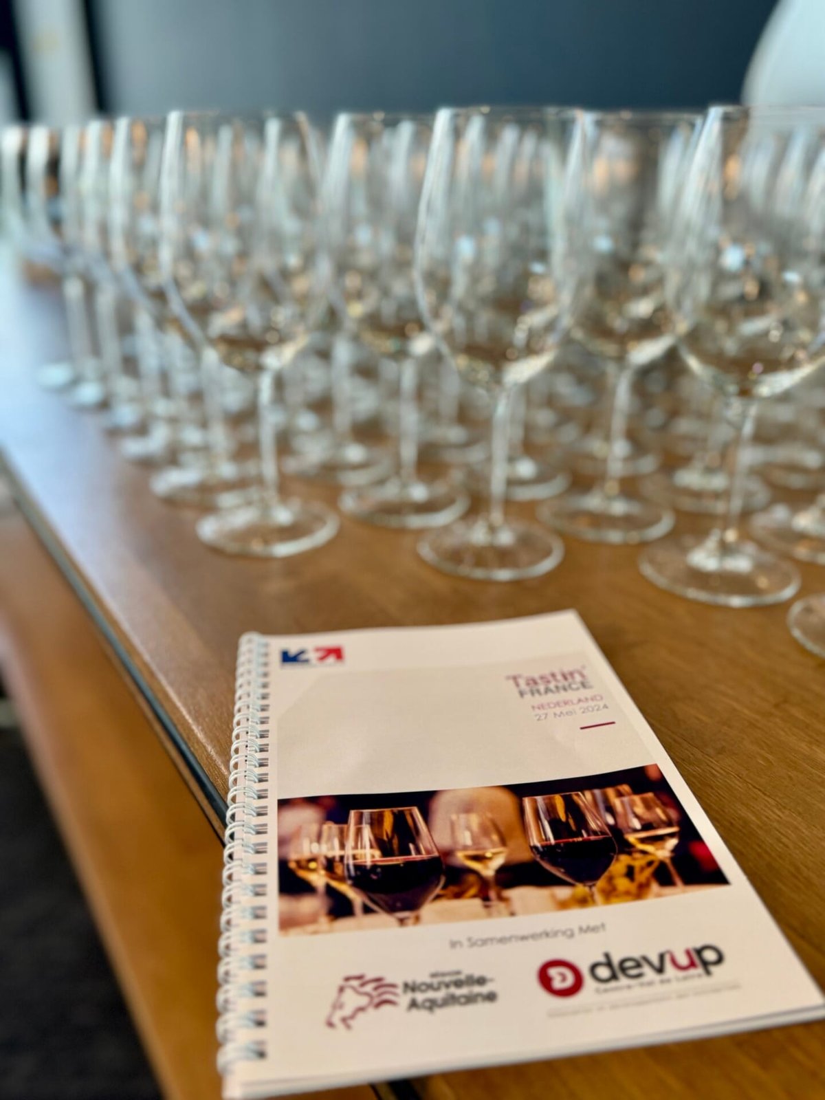 Tastin' France 2024 programmaboekje op een houten tafel voor een rij lege wijnglazen