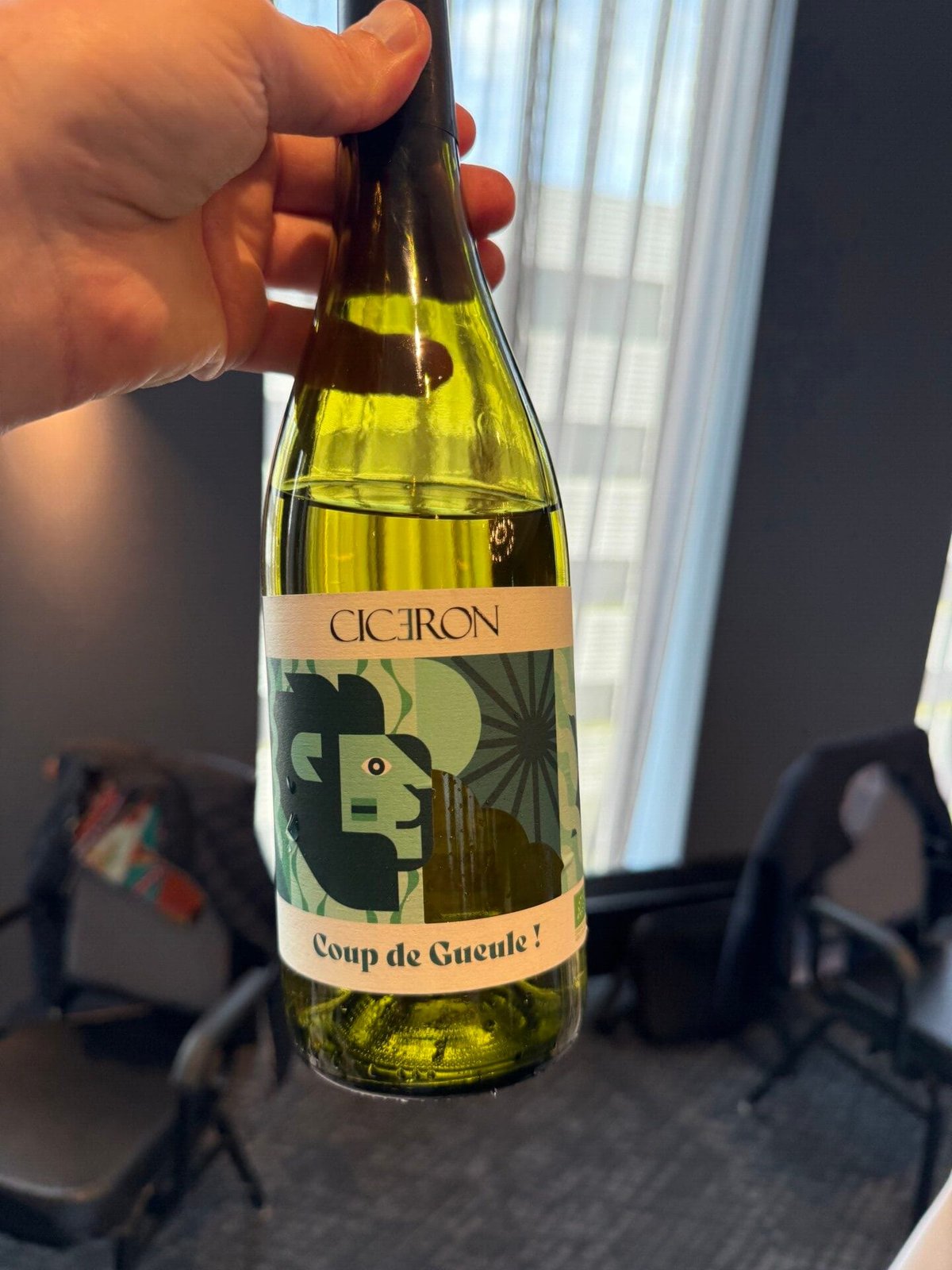 Hand houdt fles Cicéron Coup de Gueule witte wijn met kleurrijk grafisch etiket vast